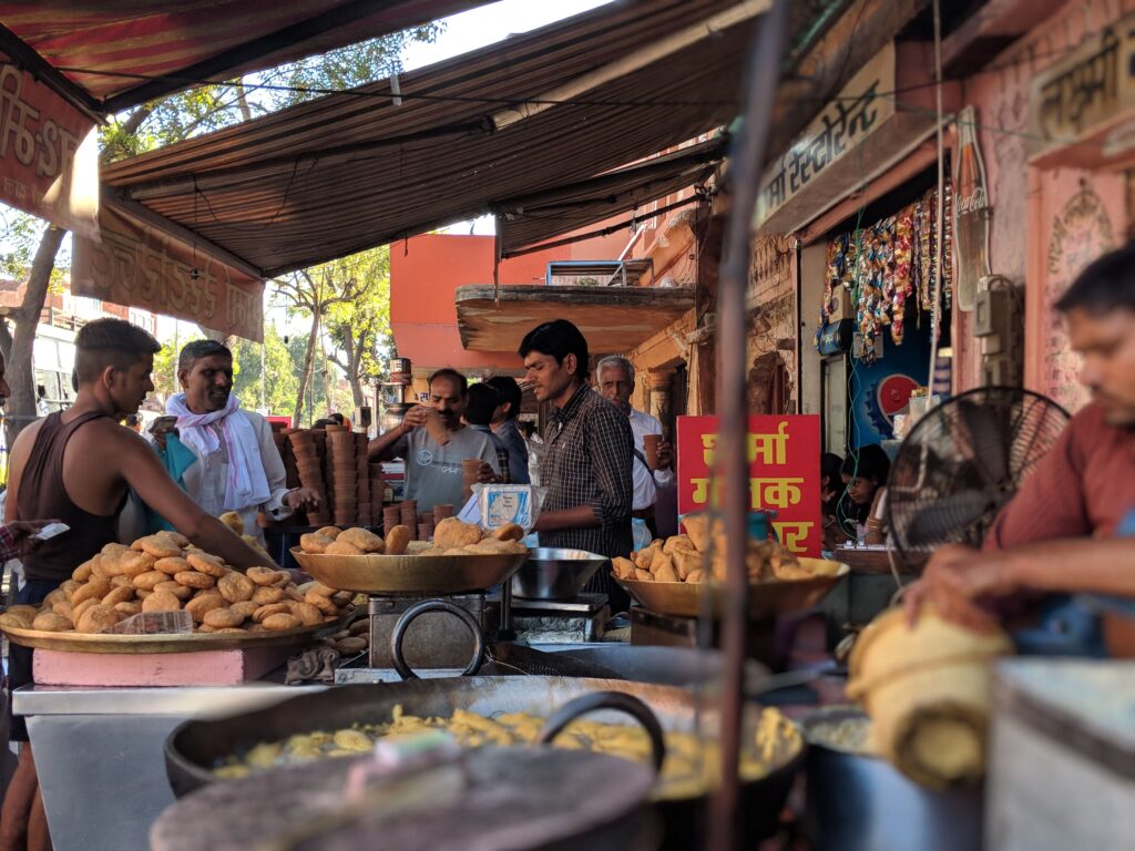 Busy street market in India with vendors selling traditional snacks and engaging with customers.